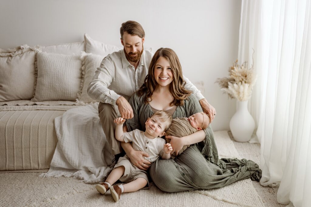 family photo with newborn baby girl and toddler big brother cuddling together in a lifestyle type photo for their newborn session in east jordan michigan