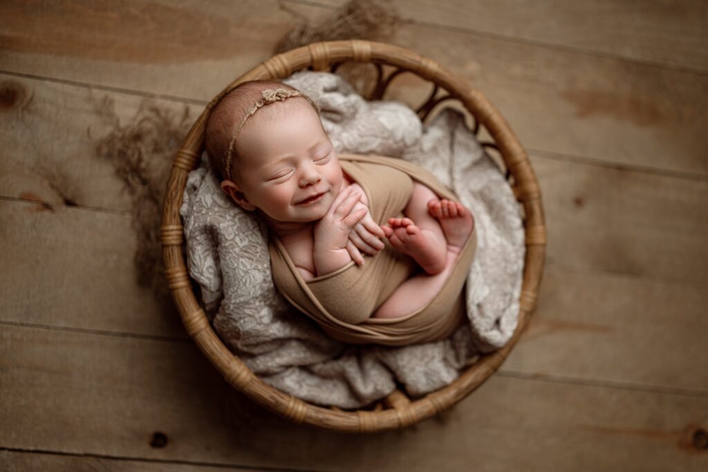 smiling newborn baby girl gently wrapped and posed for her newborn session at east jordan photography studio